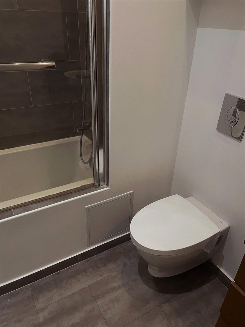 WC suspendu posé avec plaque de commande encastrée, à côté d'une baignoire
